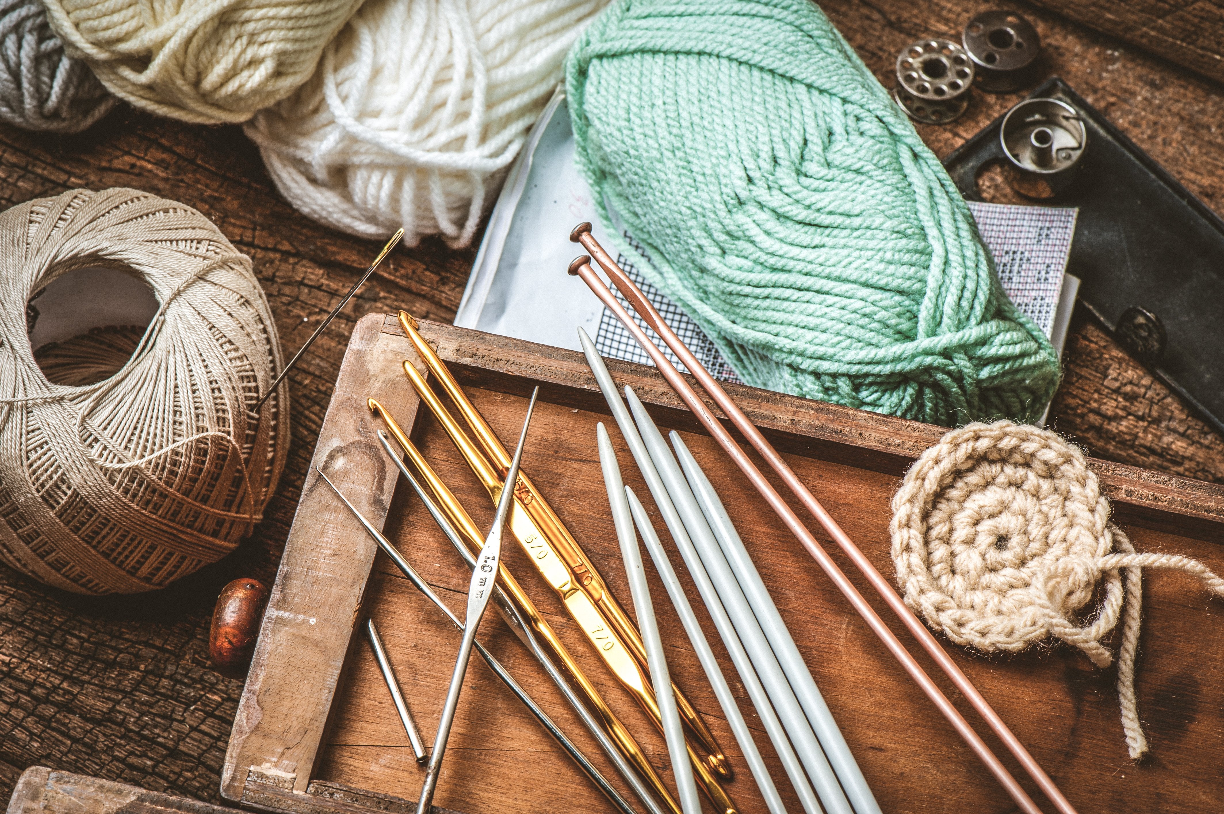 Knitting needles, crochet hooks and assorted yarn displayed on a wooden tray.